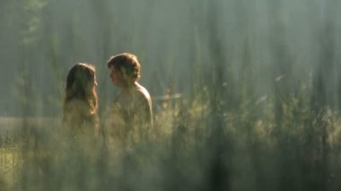 Beautiful naked couple in love holds hands and softly kisses on the green mountain open meadow at sunset