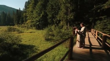 Geleneksel Ukrayna giysileri Mutlu güzel çift yumuşak öpüşme ve Karpat dağlarında ahşap köprü üzerinde eğlenmek. Comera yavaş çekimde hareket eder