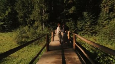 Beautiful and happy couple dances on the wooden bridge. Young man and woman in love on background of Carpathian mountains