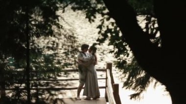 Side view of happy young couple standing on edge of pier by lake in mountains. Carpathians, Ukraine