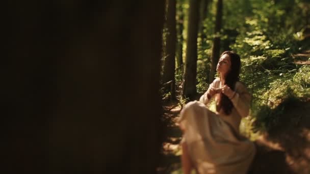 Gentle young girl sitting barefoot in the carpathian woods and combing her braids — Stock Video