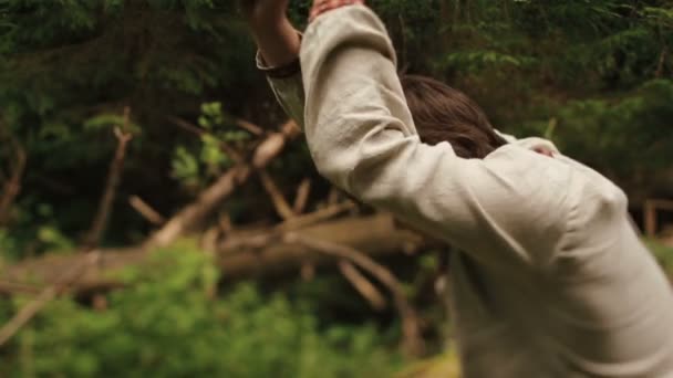 Young countryman woodcutter in traditional ukrainain clothes chopping wood in the green forest of Carpathian mountains — Stock Video