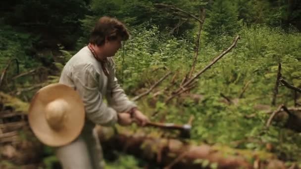 Young countryman woodcutter in traditional ukrainain clothes chopping wood in the green forest of Carpathian mountains — Stock Video