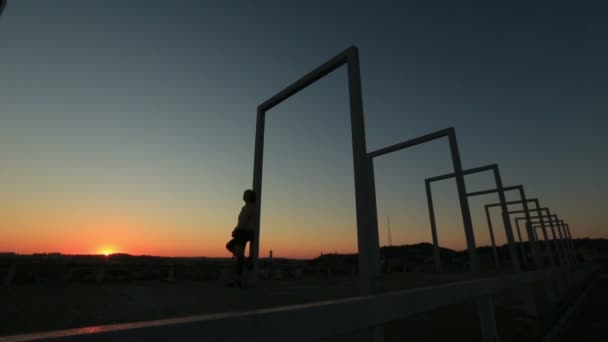 Силуэт одинокой женщины, стоящей на высокотехнологичном мосту на красном закате — стоковое видео