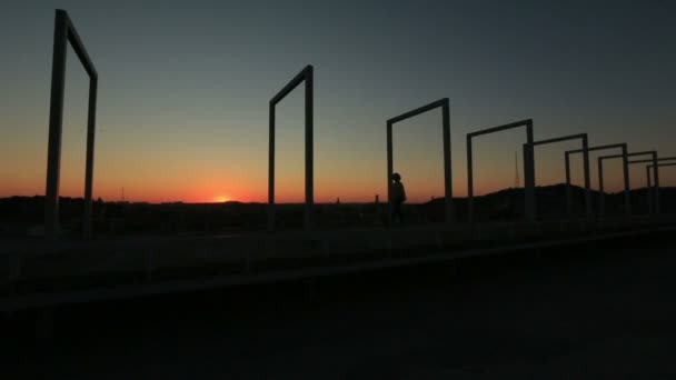 Силует самотньої жінки, що йде сама на високотехнологічному мосту на червоному заході сонця — стокове відео
