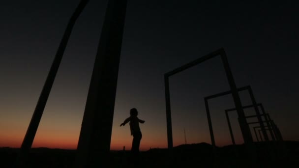 Silhouette eines jungen verträumten Mädchens, das auf die Stadtbrücke springt und die Hände hebt. Hintergrund Sonnenuntergang — Stockvideo