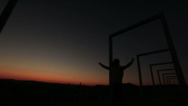 Silhouette eines jungen verträumten Mädchens, das auf der Stadtbrücke springt und Spaß hat und die Hände hebt. Hintergrund Sonnenuntergang — Stockvideo