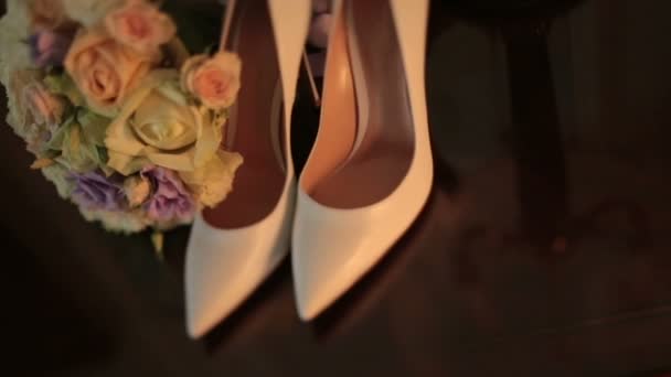 Luxus fehér bőr női magas sarkú cipő mellett a gyönyörű rózsák csodálatos színes esküvői csokor az asztalon. — Stock videók