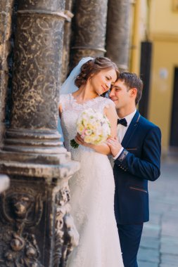 Eski bina sütunlar arasındaki alnına dokunmak duygusal romantik damat sarılma güzel gelini arkadan,