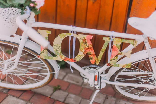 Vélo blanc décoratif avec panier de fleurs et mot amour, intérieur — Photo