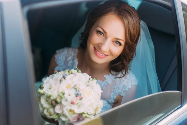Happy smiling bride with flower bouquet siting in the car — Stock Photo, Image