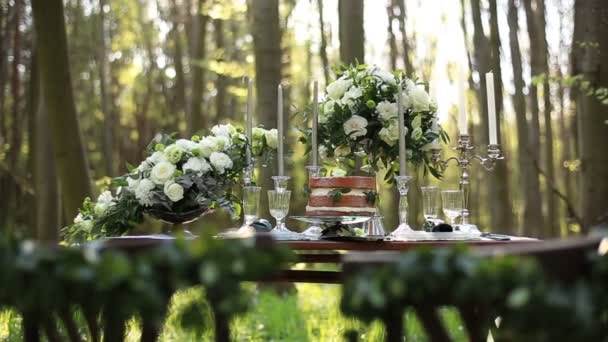 Hermosa mesa decorada de boda establecida para dos en la naturaleza en el bosque. Boda decoración de ramos de rosas blancas y candelabro vintage cerca de la torta de chocolate — Vídeo de stock