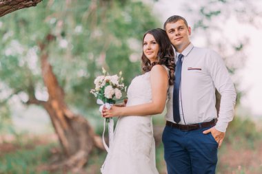 Güzel gelin gelin buketi ve doğru yeşil park arka plan üzerinde seyir poz damat ile