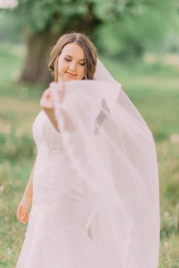 Örtü, arka plan bahar yeşil park ile oynayan beyaz elbiseli güzel gelin