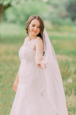 Örtü, arka plan bahar yeşil park ile oynayan beyaz elbiseli güzel gelin