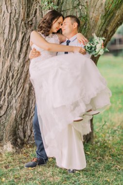 Güzel eşi büyük ağaç bahar yeşil Park yakınındaki taşıyan genç gülümseyen damat