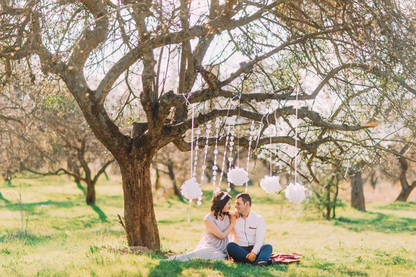Φωτογραφία συνόδου εμπλοκή του όμορφο ζευγάρι στην αγάπη που κάθεται στο καρό. Διακοσμημένο κήπο με σύννεφα — Φωτογραφία Αρχείου