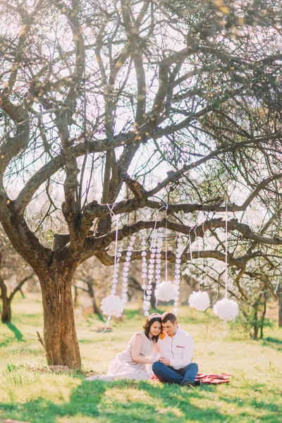 Обручальная фотосессия прекрасной влюбленной пары, сидящей на клетке. Украшенный садом с облаками — стоковое фото