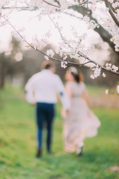 Coppia felice che corre in giardino fiorito tenendosi per mano — Foto Stock