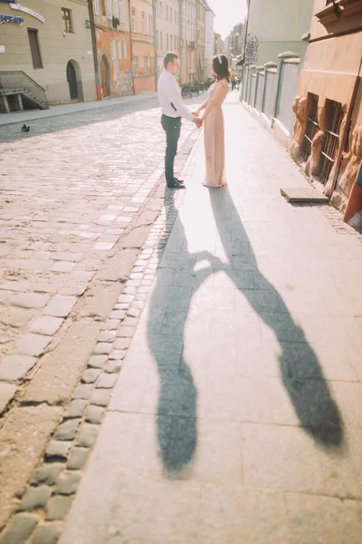 Διασκεδαστικό ζευγάρι, νύφη και τον γαμπρό, κρατώντας τα χέρια στον παλιό δρόμο στο ηλιοβασίλεμα — Φωτογραφία Αρχείου