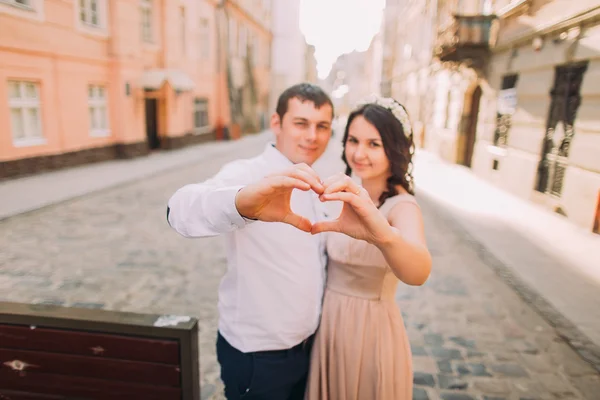 Усміхнена пара формує форму серця своїми руками на старій вулиці — стокове фото