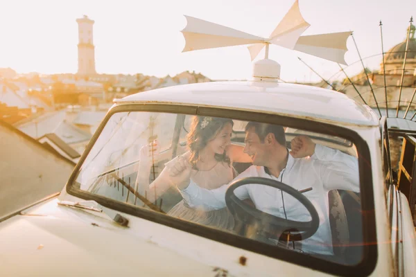 Mladý pár žena nosí květinovou čelenku a pohledný muž, pózuje v bílé retro auto na střeše — Stock fotografie