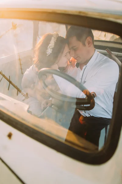 Retrato de chica joven con diadema floral y hombre guapo sentado en coche vintage sonriendo cara a cara — Foto de Stock