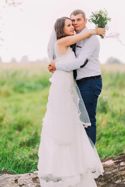 Красивая молодая супружеская пара, невеста в белом платье и красивый жених позирует на стволе дерева — стоковое фото