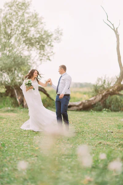 Счастливая стильная невеста с элегантным танцем грума на фоне красивых деревьев в парке — стоковое фото