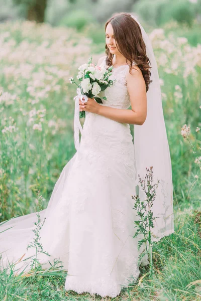 Vackra eleganta brud i bröllopsklänning holding och tittar på lyxiga naturliga vit brudbukett — Stockfoto