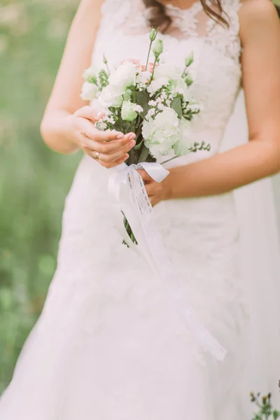 Närbild av elegant brud i bröllopsklänning holding och tittar på lyxiga naturliga vit brudbukett — Stockfoto