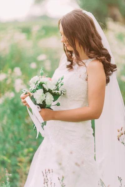 Potret close-up dari pengantin wanita cantik yang elegan dengan gaun pengantin memegang dan melihat buket pengantin putih alami yang mewah — Stok Foto