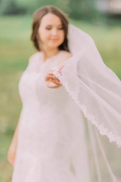 Schöne Braut im weißen Kleid, die mit Schleier spielt, frühlingshafter grüner Park auf dem Hintergrund — Stockfoto