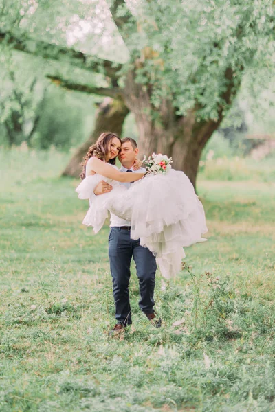 Junger lächelnder Bräutigam mit seiner schönen Frau im frühlingshaften grünen Park — Stockfoto