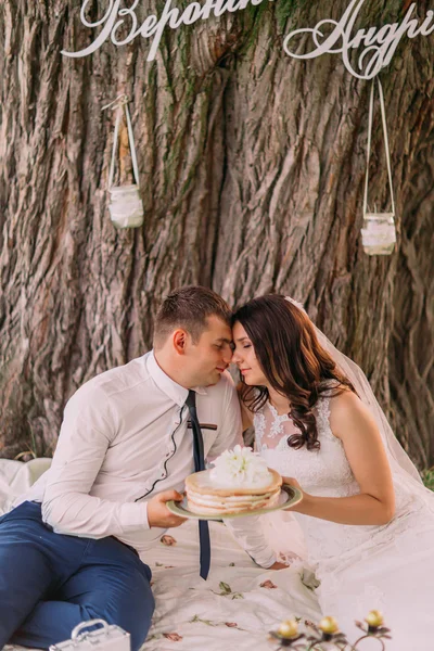 Close-up de belo casal de casamento no piquenique segurando bolo em um fundo de árvore no parque da primavera — Fotografia de Stock