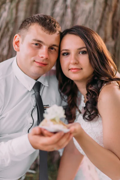 Sposo e sposo guardando la fotocamera che tiene pezzo della loro torta nuziale, primo piano — Foto Stock