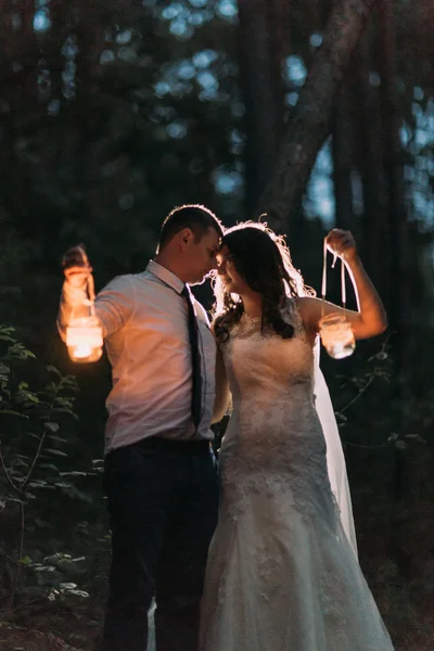 Glückliches Ehepaar mit Kerzenlaterne, die sich vor dem Hintergrund des dämmrigen Waldes anschauen — Stockfoto