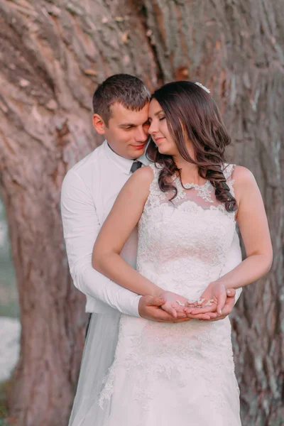 Joven novia y novio en un abrazo, manos con anillos de boda dorados, letras de madera en el estómago de las mujeres — Foto de Stock