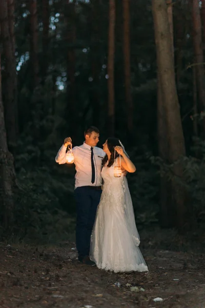 Feliz pareja casada con linterna de vela mirándose el uno al otro en el fondo del bosque crepuscular — Foto de Stock
