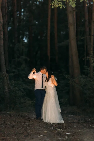 Feliz pareja casada con linterna de vela mirándose y besándose en el fondo del bosque crepuscular —  Fotos de Stock