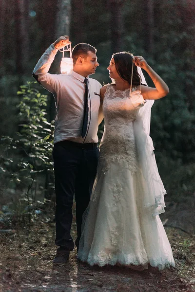 Gelukkig getrouwd stel met kaars lantaarn kijken elkaar op achtergrond van twilight bos — Stockfoto