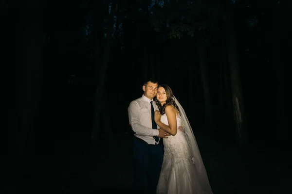 Adorning elegant fashion groom and bride embracing looking at camera on the night background — 图库照片