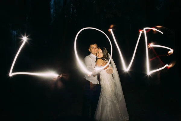 Embracing married couple and light painting of the word Love on background