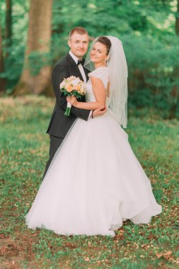 Yeni evli gelin gelin buketi ve doğa yeşil ormanda kucaklayan damat ile