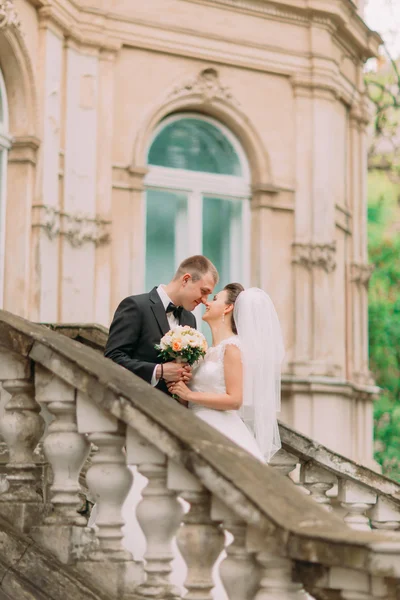 Linda pareja casada tocando narices de cerca de pie en el balcón antiguo con columnas —  Fotos de Stock