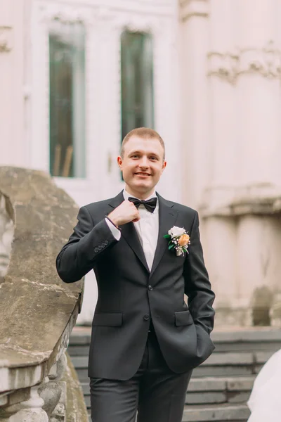 Feliz, novio recién casado sonriente posando frente a viejas escaleras en un traje de blck — Foto de Stock