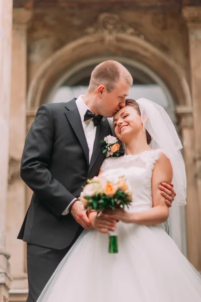 Крупным планом фотография счастливого жениха целующего невесту в лоб на заднем плане старого здания — стоковое фото