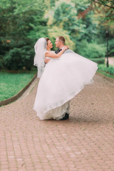 Junger Bräutigam trägt seine schöne Frau im Sommerpark — Stockfoto