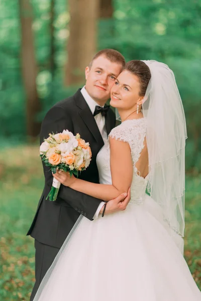 Nygifta bruden med brudbukett och brudgummen embracing i naturen grön skog — Stockfoto