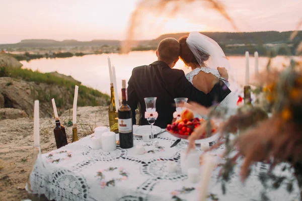 Fiatal esküvői pár siiting vissza a tó romantikus este a gyertyák, a homokos strand — Stock Fotó